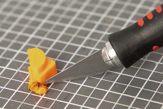 Skalpell schneidet Kunststoffrest von einem 3D Druck Bauteil weg