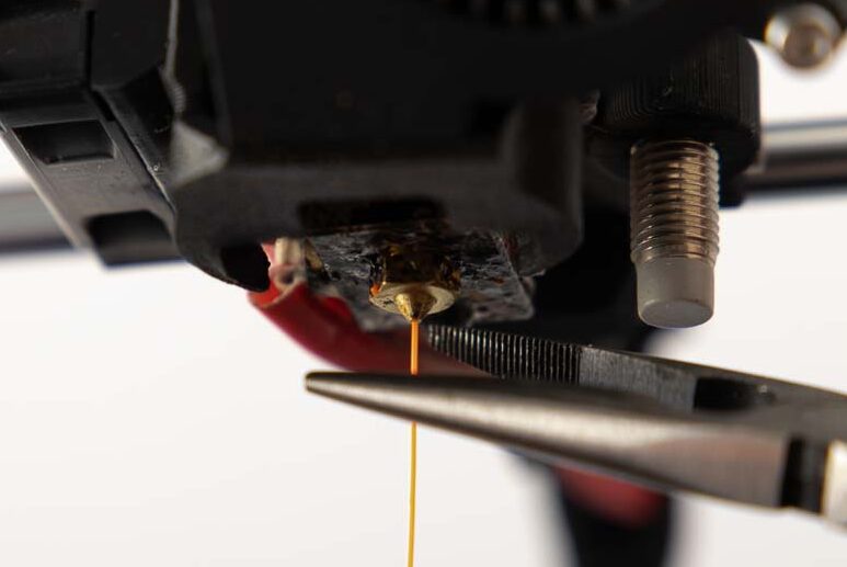 Mini Spitzzange setzt an der Düse an umd den 3D Drucker vom überschüssigen Filament zu befreien