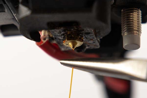 Mini needle-nose pliers remove the excess filament from the 3D printer