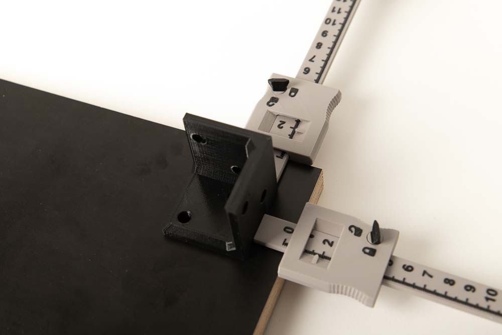 Three-sided bracket on wooden panel is positioned using 2 depth calipers