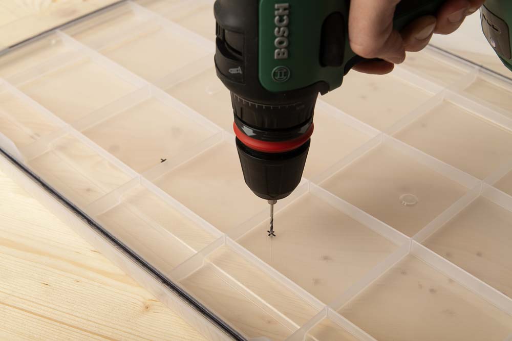 A hole is drilled in the lid of the Iris 50l box with a cordless screwdriver and a 2 mm wood drill bit.