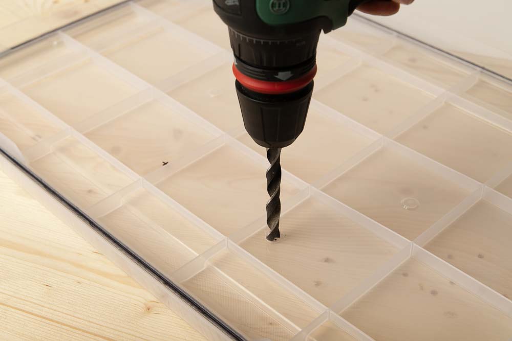 A hole is drilled in the lid of the Iris 50l box with a cordless screwdriver and a 10 mm wood drill.