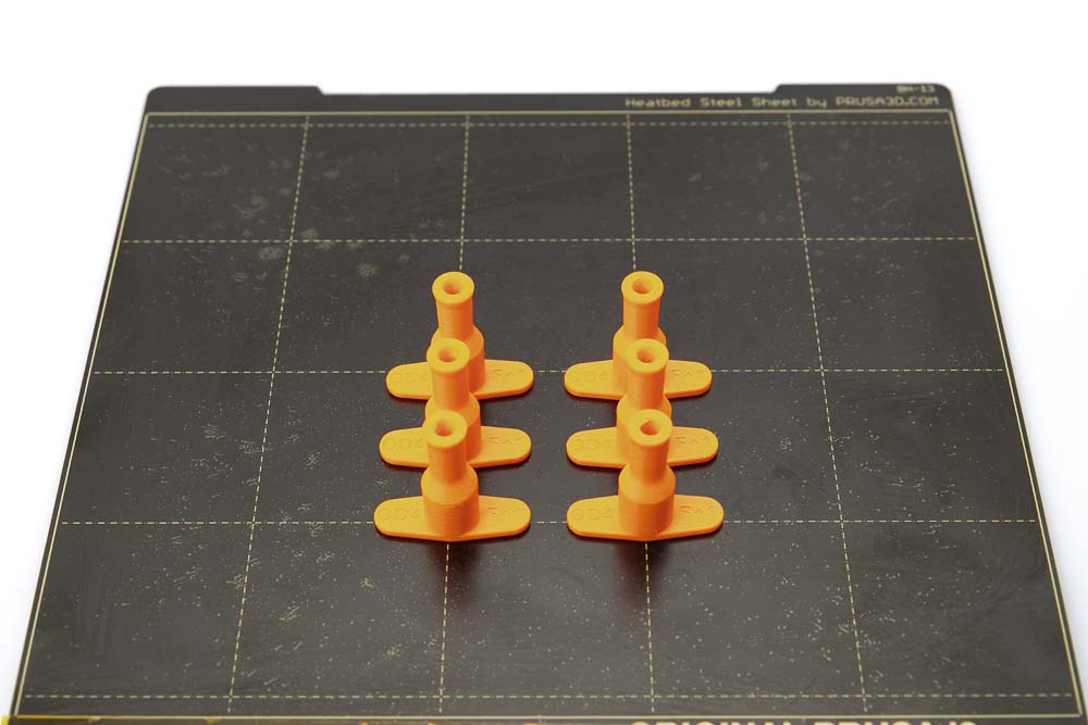 Build plate of the Prusa i3 MK3S on which 6 pieces of 3D printed tube plugs for variant A lie. All parts are printed in orange PETG filament with a layer height of 0.2 mm.