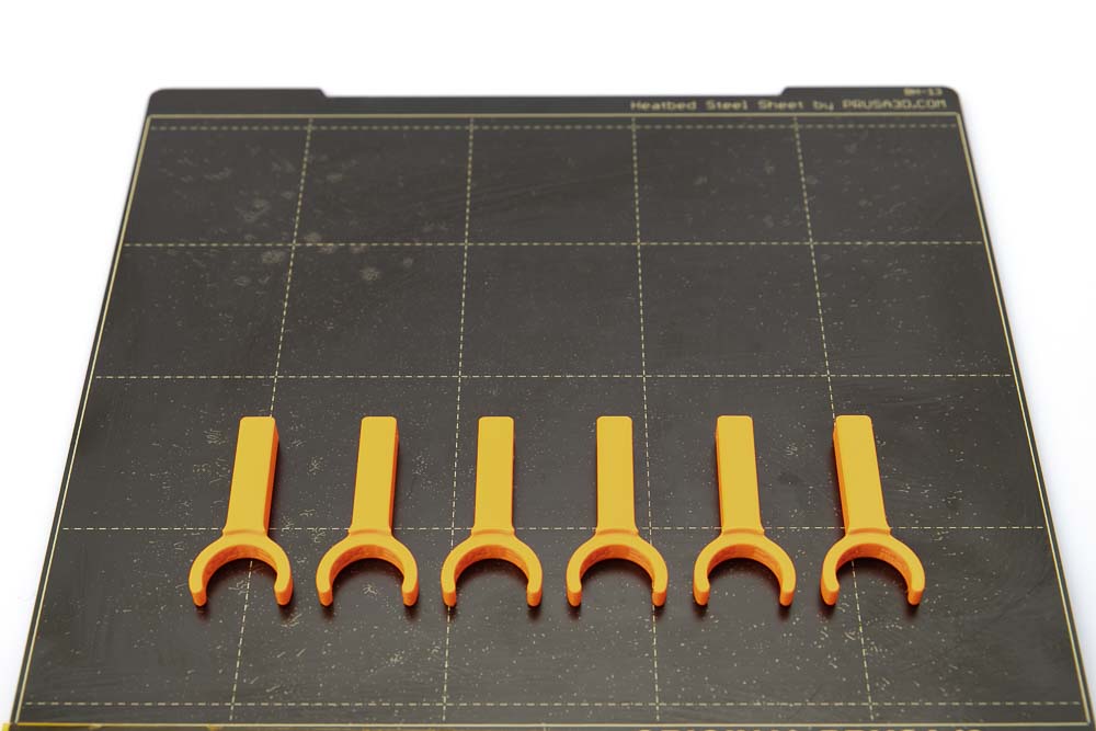 Druckplatte des Prusa i3 MK3S auf der 6 Stück 3D gedruckte Schlauch-Stoppel für Variante B liegen. Alle Teile sind in orangen PETG Filament mit einer Schichthöhe von 0,2 mm gedruckt.