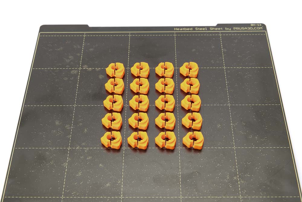 Spring steel build plate of the Prusa i3 Mk3S with 20 pieces of 3D printed quick-lock nuts in orange PETG.
