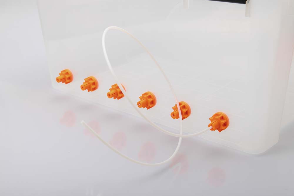 Luftdichte 50L Kunststoffbox mit sechs orangen Filament Durchführungen, alle mit einer 3D gedruckten Mutter gesichert. In der ersten Durchführung steckt ein langes (90 cm) Stück PTFE Schlauch.
