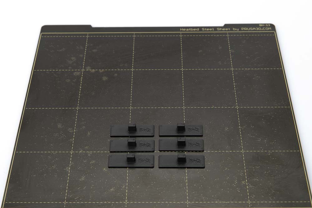 Druckplatte des Prusa i3 MK3S auf dem 6 schwarze Kontrastplatten liegen. Die Platten wurden in schwarzen matten PLA Filament mit einer Schichthöhe von 0,2 mm gedruckt.