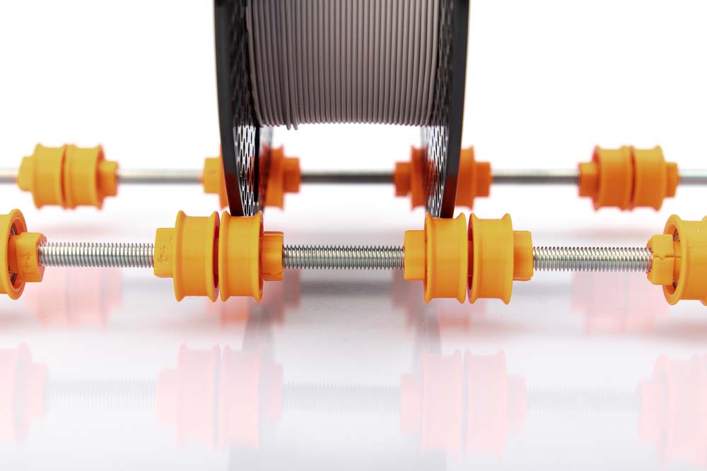 Eine Filament Spule steht auf kugelgelagerten, 3D gedruckten Einzelrollen die auf einer M8 Gewindestange auf gefädelt sind.