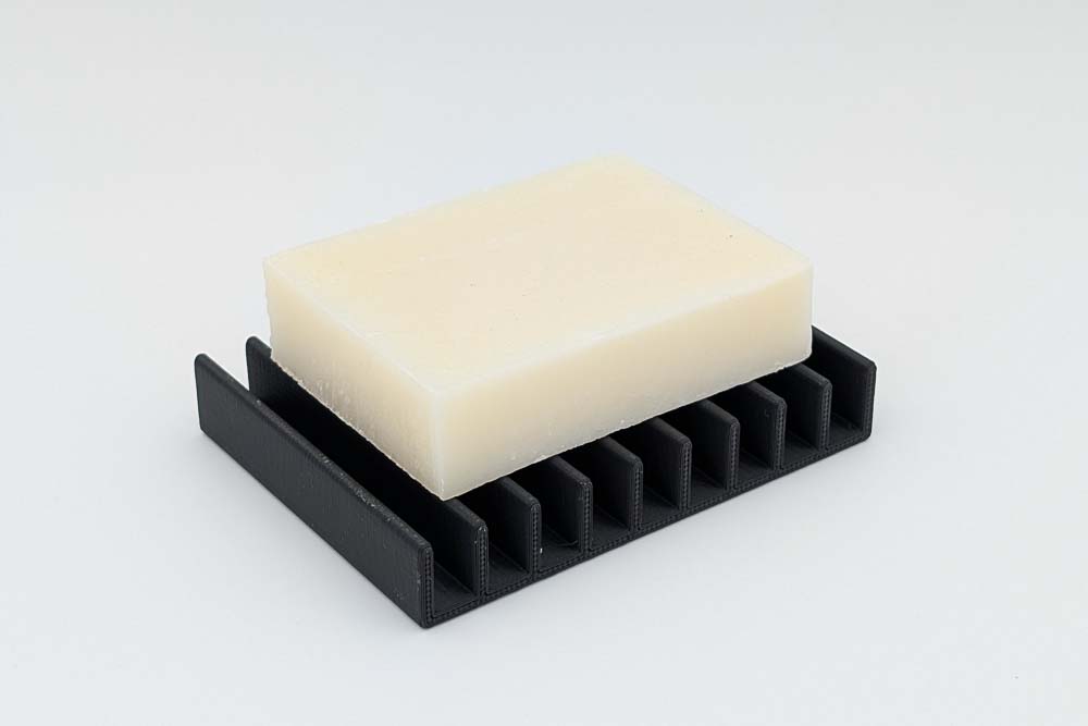 3D Druck Seifenschale, gedruckt in matt schwarzen Filament, zeigt das Design Rippen und eine darauf platzierte Seife